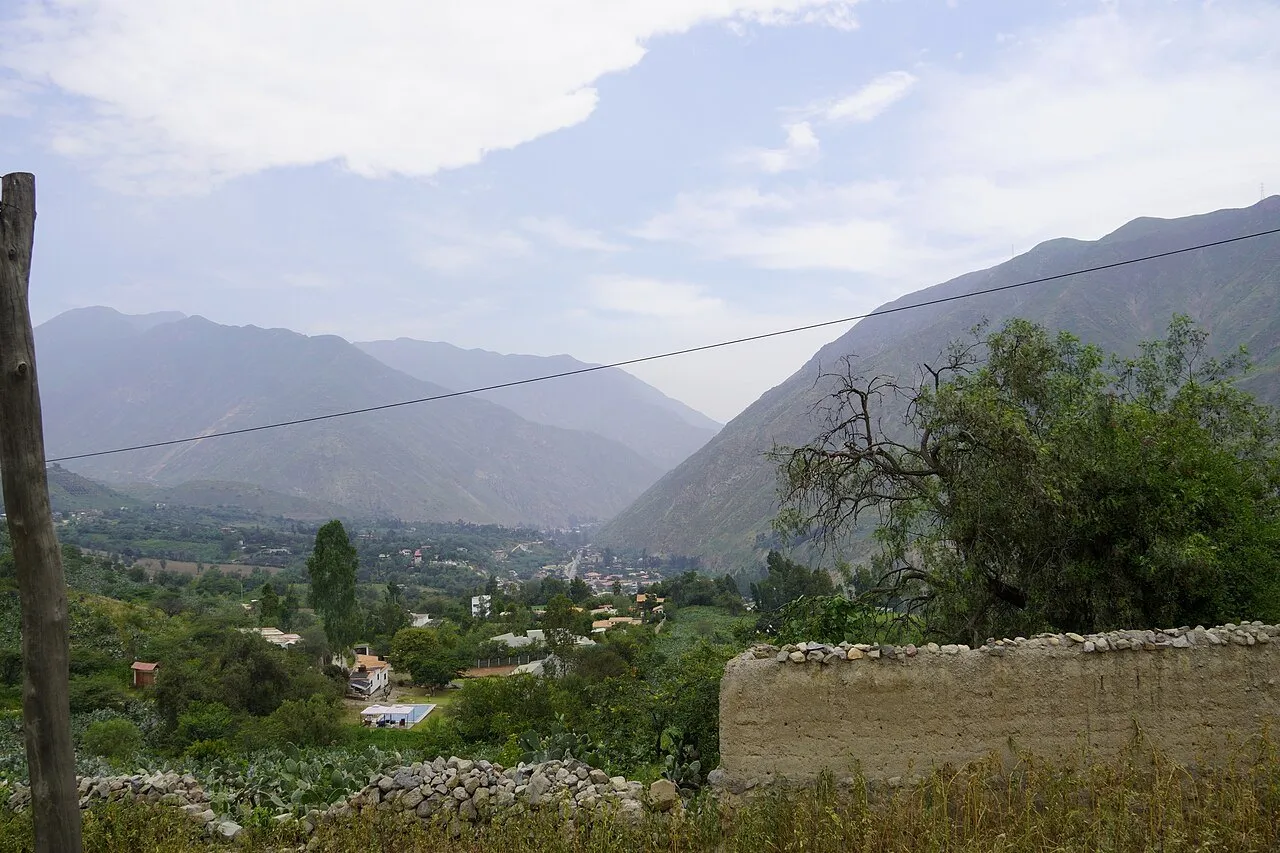 An Andean valley with green mountains and houses among trees in Huarochirí province, Lima
