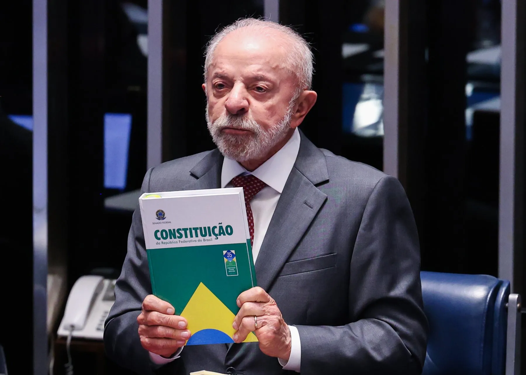 Luiz Inácio Lula da Silva, in a grey suit, holds up a copy of Brazil's Constitution in the Senate chamber