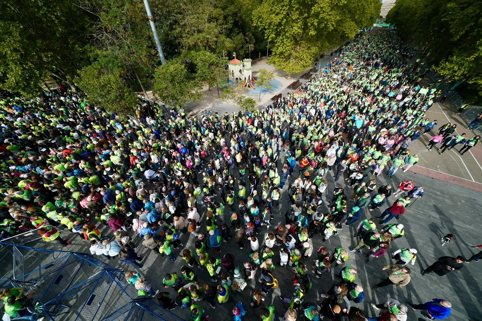 Aerial view of thousands of walkers in green T-shirts filling a whole avenue next to a children's playground