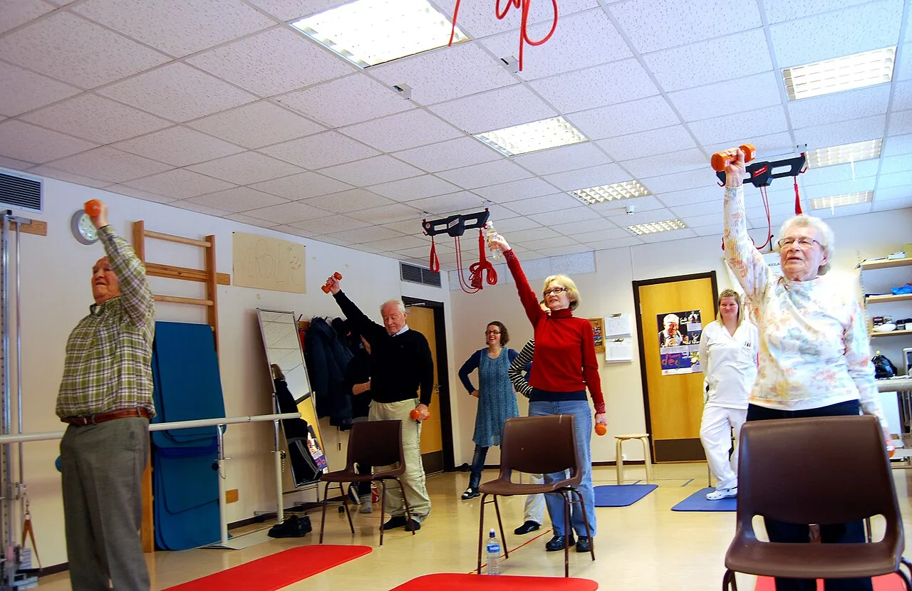 A group of older people lifting small weights above their heads in an exercise room