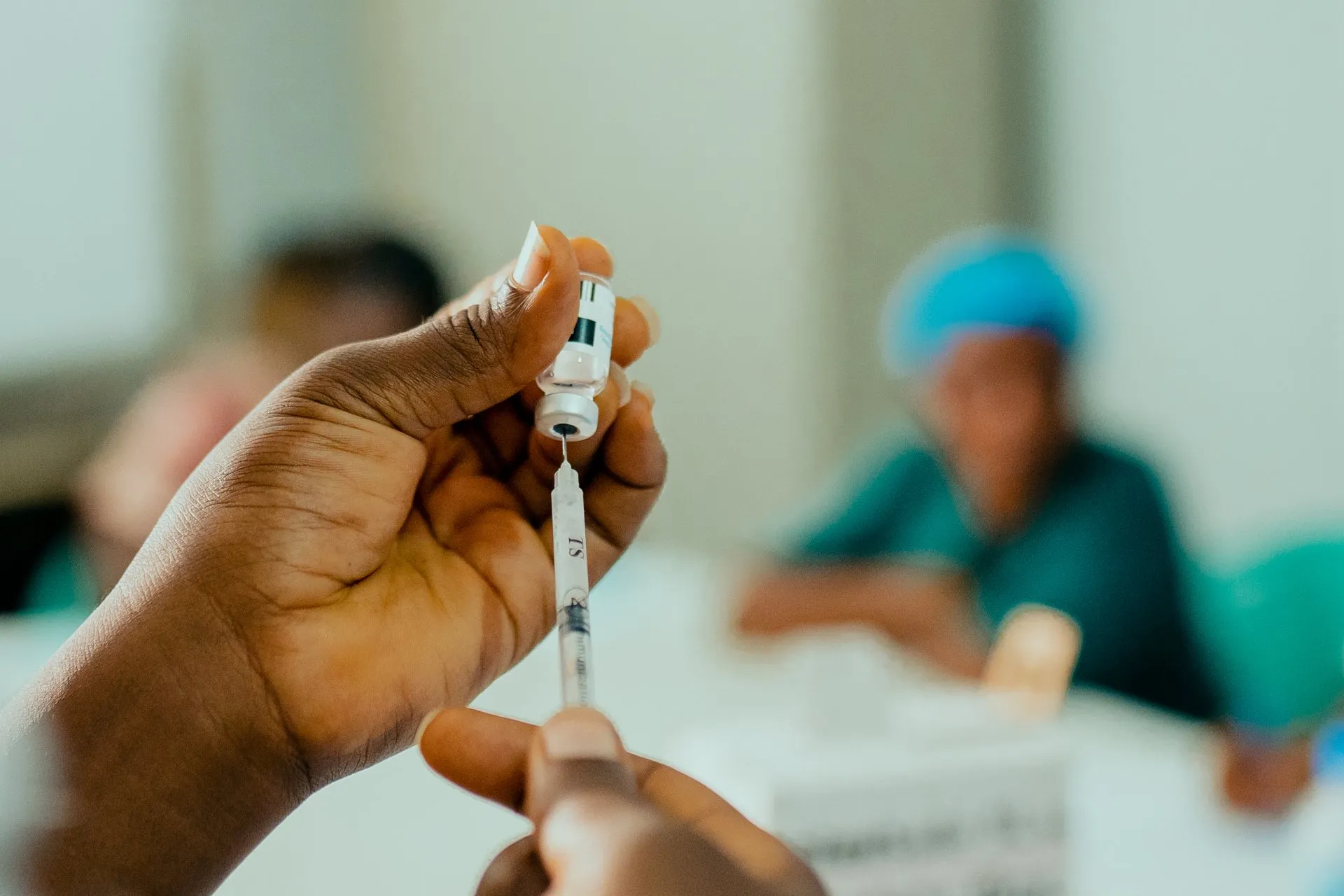 A health worker draws mpox vaccine from a vial into a syringe, with another health worker out of focus in the background