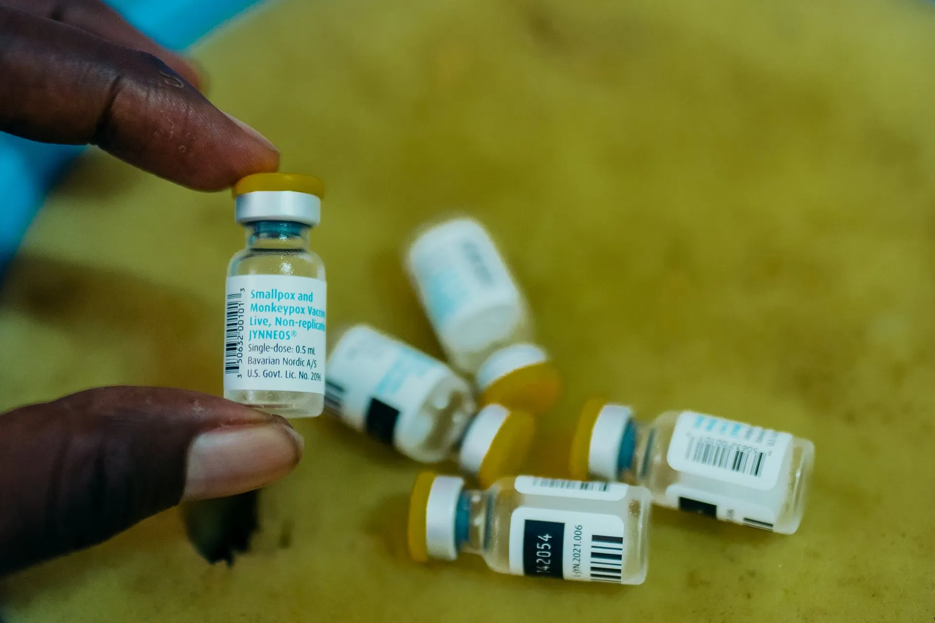 Several vials of mpox vaccine on a table, one of them held between two fingers