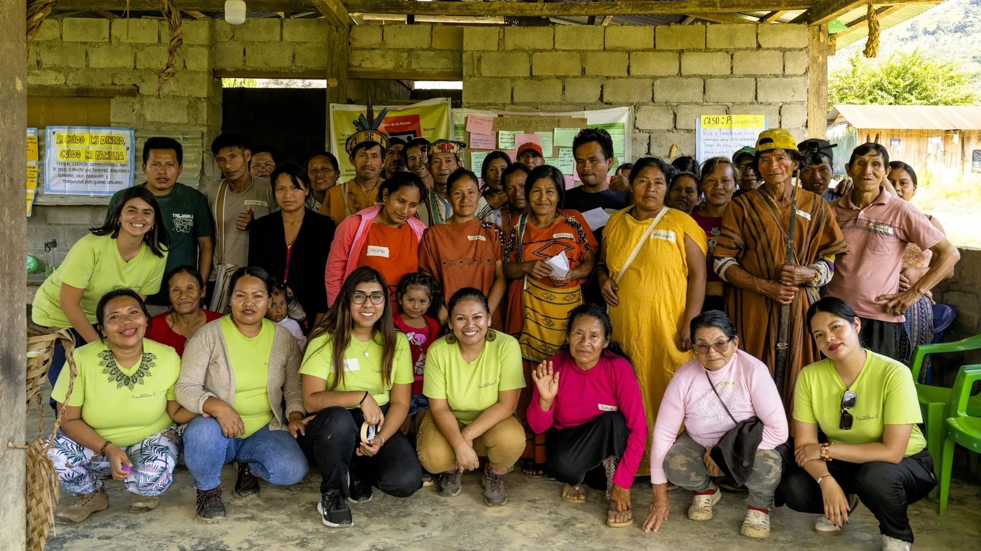 A large group of community members, some in traditional cushmas, pose with the programme team in green T-shirts