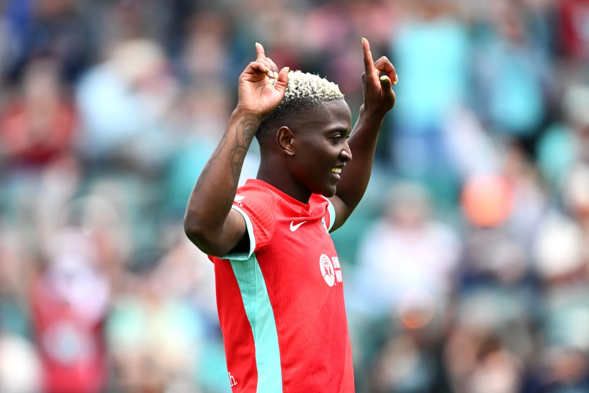 Temwa Chawinga, in the red Kansas City Current shirt, smiles and points both index fingers to the sky in a packed stadium